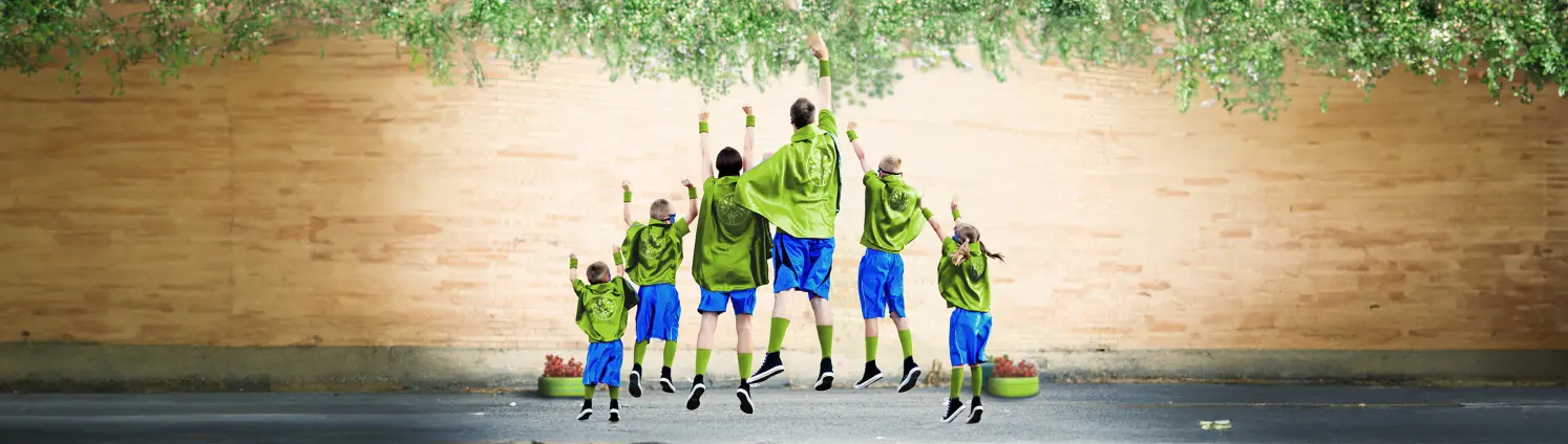 Familie, die als Superhelden in grün gekleidet, sind von hinten zu sehen und machen eine Superman-Pose