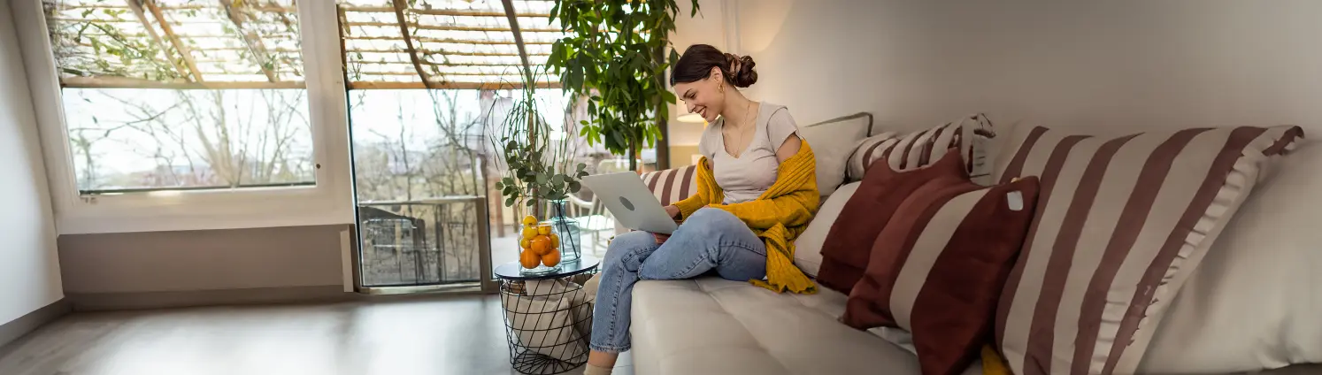 Eine junge Frau sitzt auf dem Sofa und schaut auf den Laptop auf ihren Knien