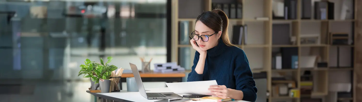 Eine Frau mit Brille sitzt am Schreibtisch und studiert Aufzeichnungen