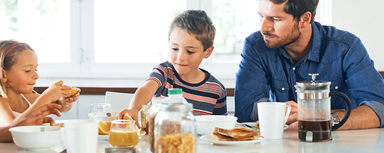 Zwei Kinder und Vater sitzen am Tisch und frühstücken