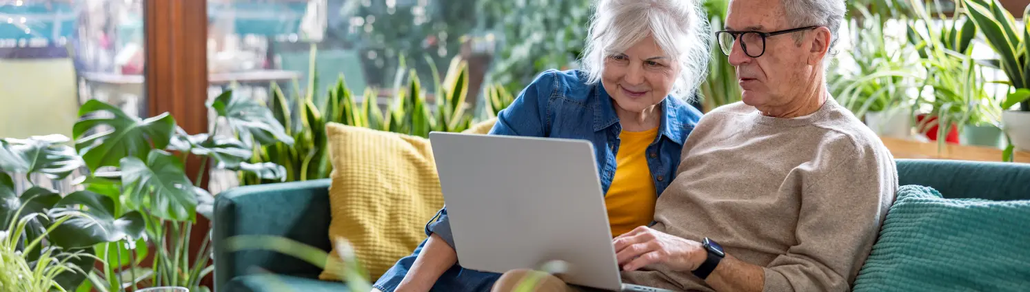 Seniorenpaar mit Laptop, während sie zu Hause auf dem Sofa im Wohnzimmer sitzen