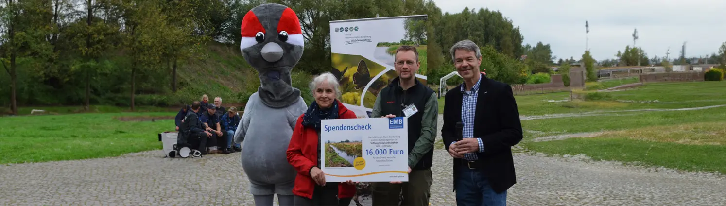 Ein Maskottchen und Personen halten einen Spendenscheck