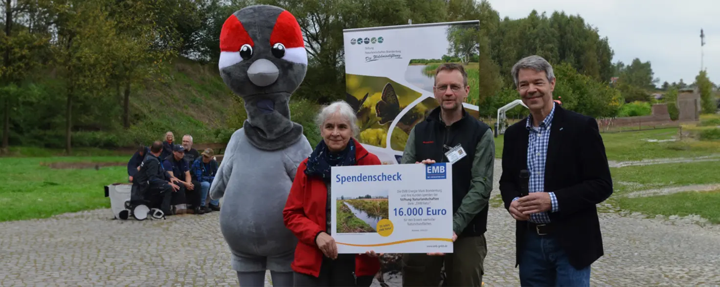 Ein Maskottchen und Personen halten einen Spendenscheck