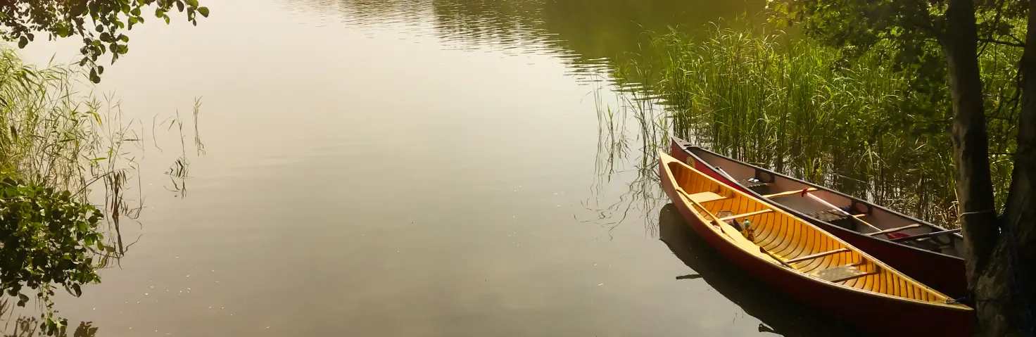 Ein See in bewaldeter Umgebung, am Rand sind zwei Kanus angeleint