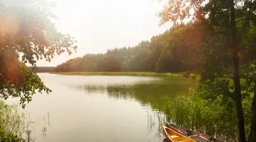 Ein See in bewaldeter Umgebung, am Rand sind zwei Kanus angeleint