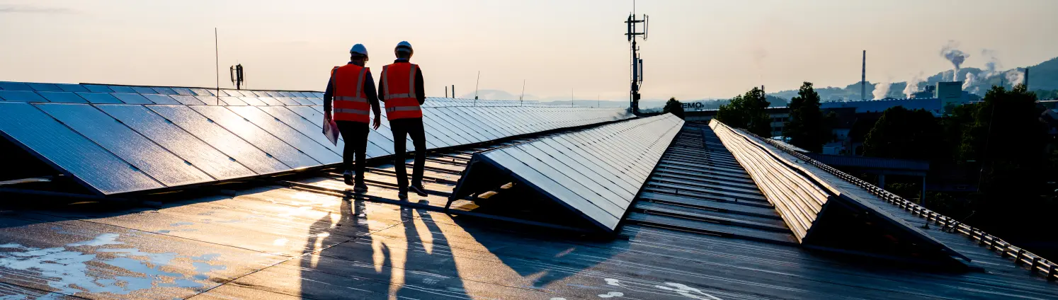 Zwei Installateure laufen über ein Dach mit Solarmodulen