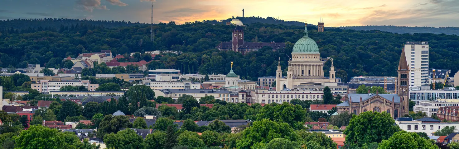 Blick auf Brandenburgs Hauptstadt Potsdam aus der Luft. Grüne Hügel und Sonnenaufgang im Hintergrund.