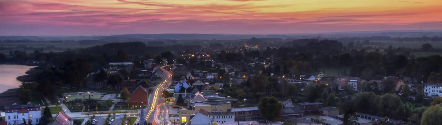 Eine Stadt am Wasser von oben fotografiert, im Hintergrund der abendliche Himmel in Rot-Tönen