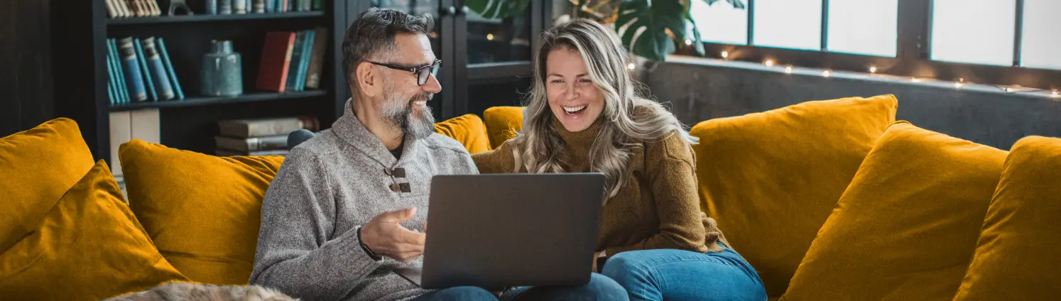 Mann und Frau sitzen mit Hund auf einem Sofa uns schauen gemeinsam auf den Laptop