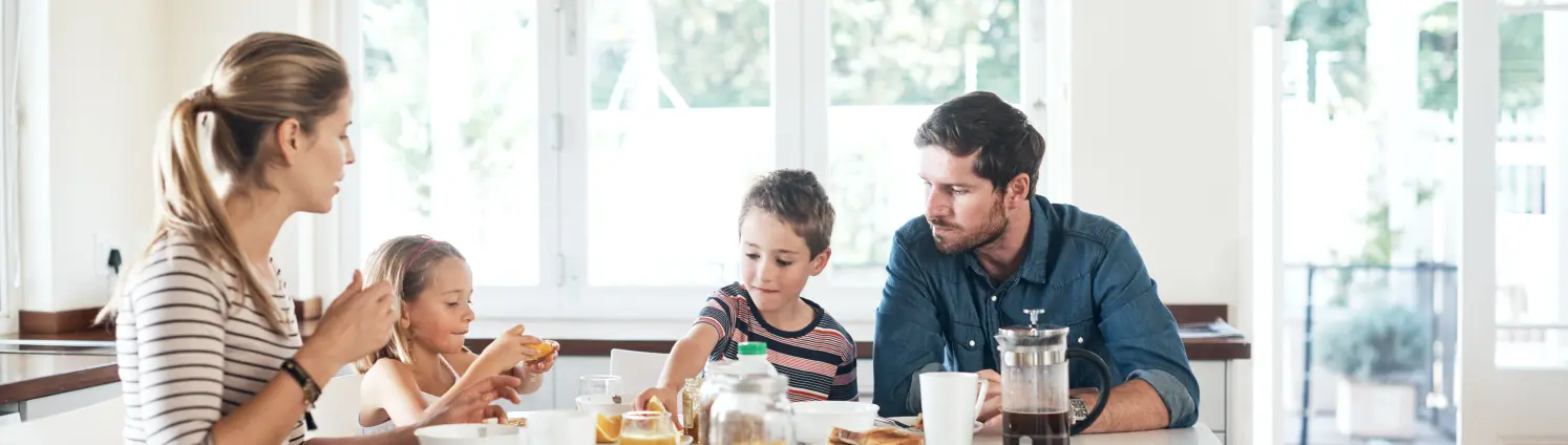 Mutter, Vater und zwei Kinder sitzen zum Frühstück an einem Tisch in einer hellen Küche