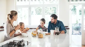 Mutter, Vater und zwei Kinder sitzen zum Frühstück an einem Tisch in einer hellen Küche