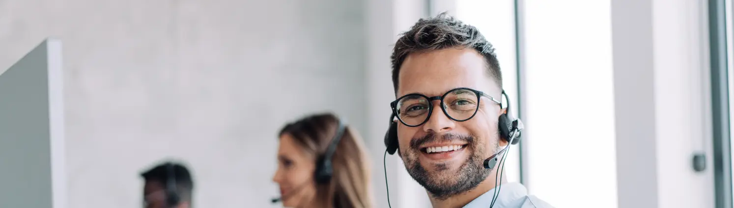 Blick in ein Kundenbüro, ein Mann mit Brille und Headset lächelt in die Kamera