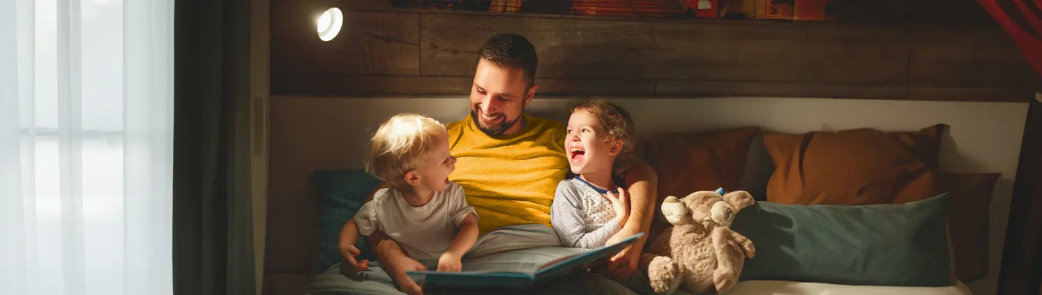 Ein Mann lächelt zwei Kindern zu, die er auf dem Schoß sitzen hat