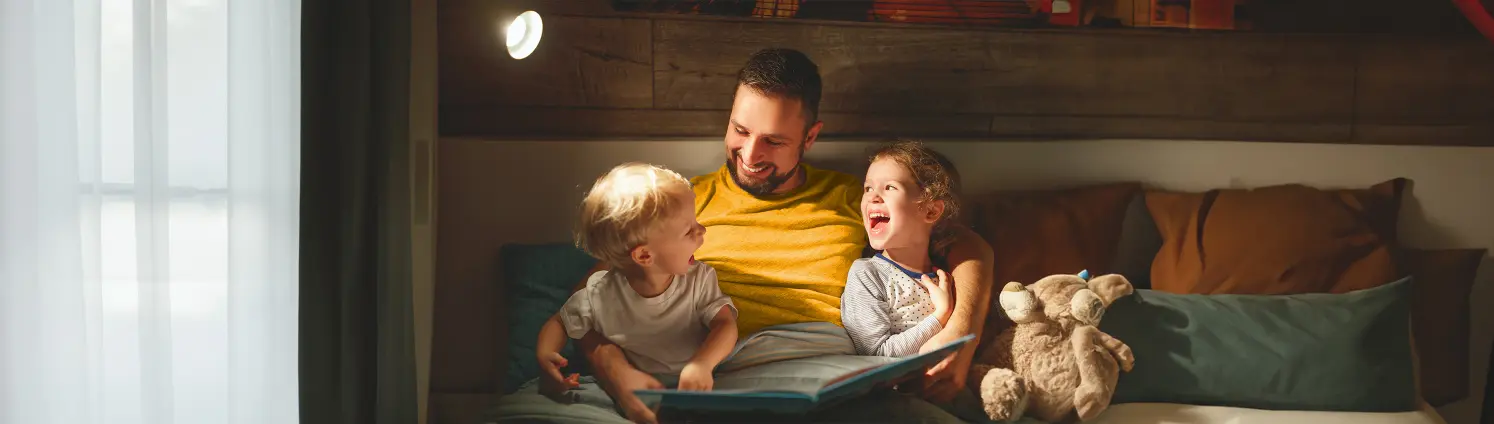 Vater sitzt gemeinsam mit zwei Kindern und liest eine Geschichte aus einen Buch vor