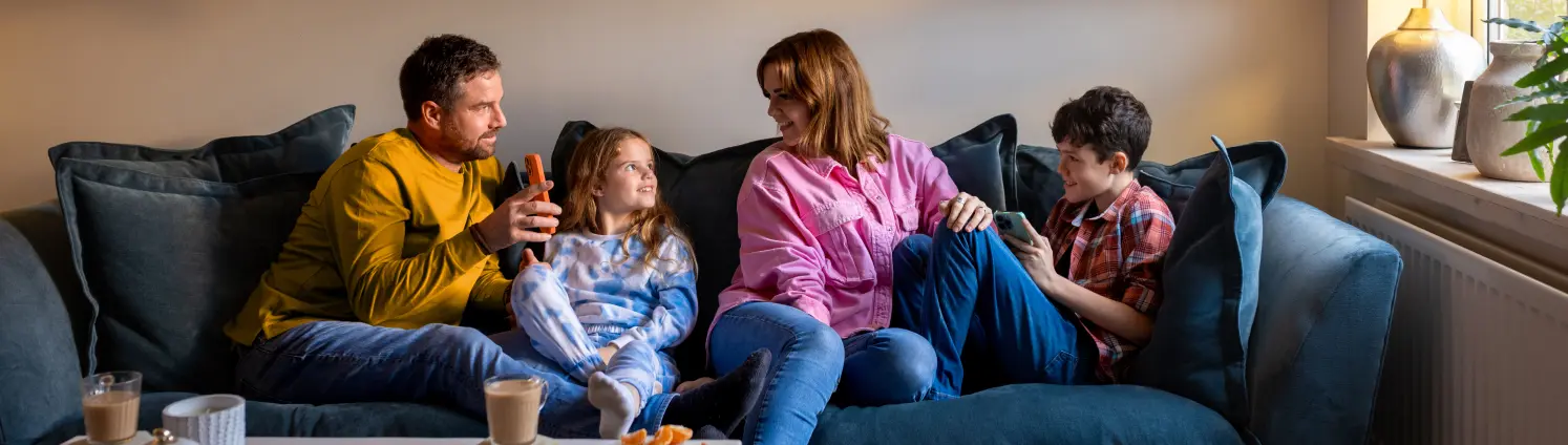 Eine Frau und ein Mann sitzen mit ihren beiden Kindern auf dem Sofa im Wohnzimmer