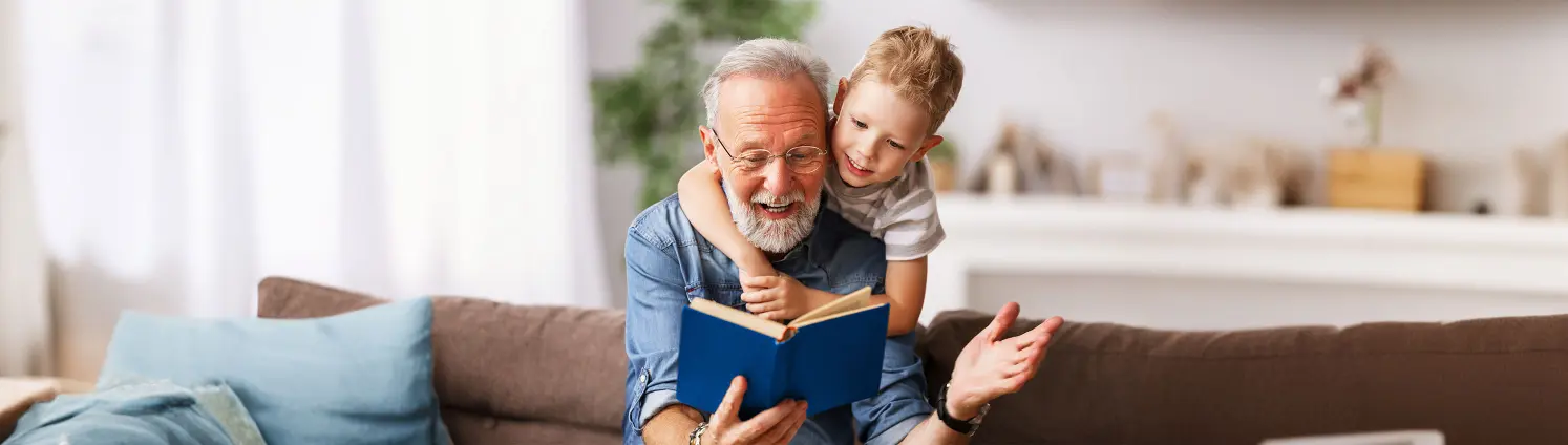 Ein Opa ließt seinem Enkel aus einem blauen Buch eine spannende Geschichte vor